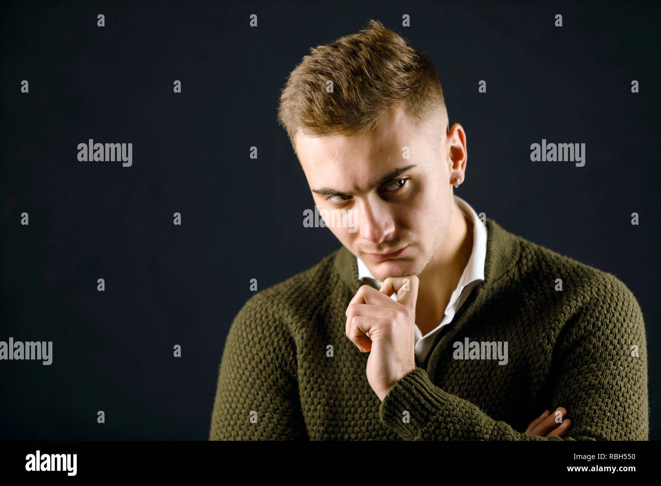Porträt der jungen Ernst stattlicher Mann mit grünen Pullover stehend auf dem grauen Hintergrund und poising im Studio Stockfoto