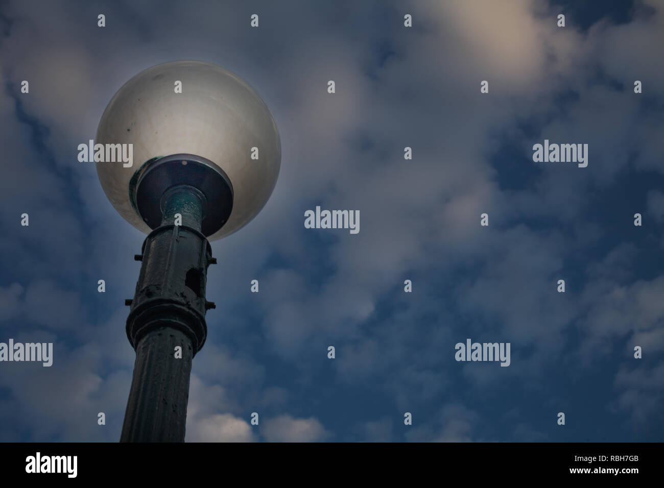 Winkel, Ansicht von Outdoor Lamp Post stehen unter Bewölkt Dim Himmel. Closeup geschossen von einer Straßenlaterne mit Runden geraucht Globe Lampe und Loch in Guss P Stockfoto