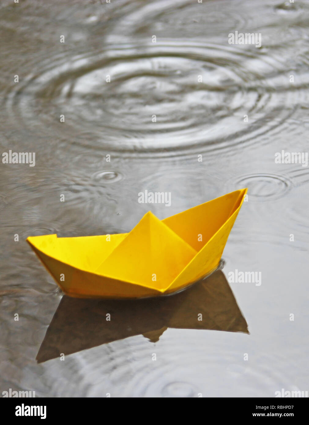 Gelbes Papier Boot schwimmen in eine Pfütze, Regentropfen ins Wasser fallen Stockfoto