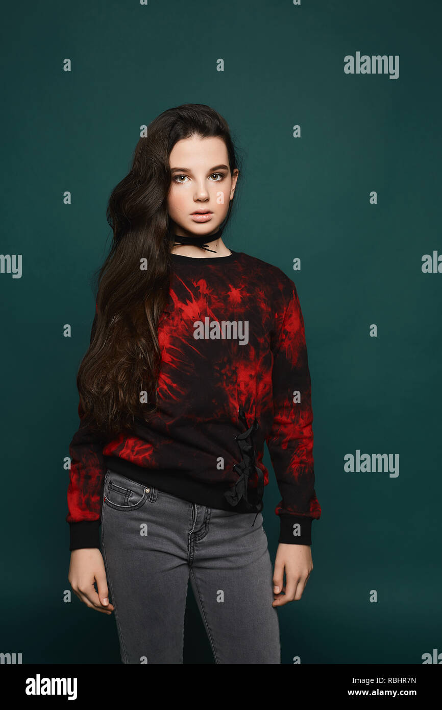 Beaytiful und modische brunette teen model Mädchen in eleganten Grau Jeans und in der schwarzen Sweatshirt mit rotem Muster an dunklen Stellen - grüner Hintergrund Stockfoto