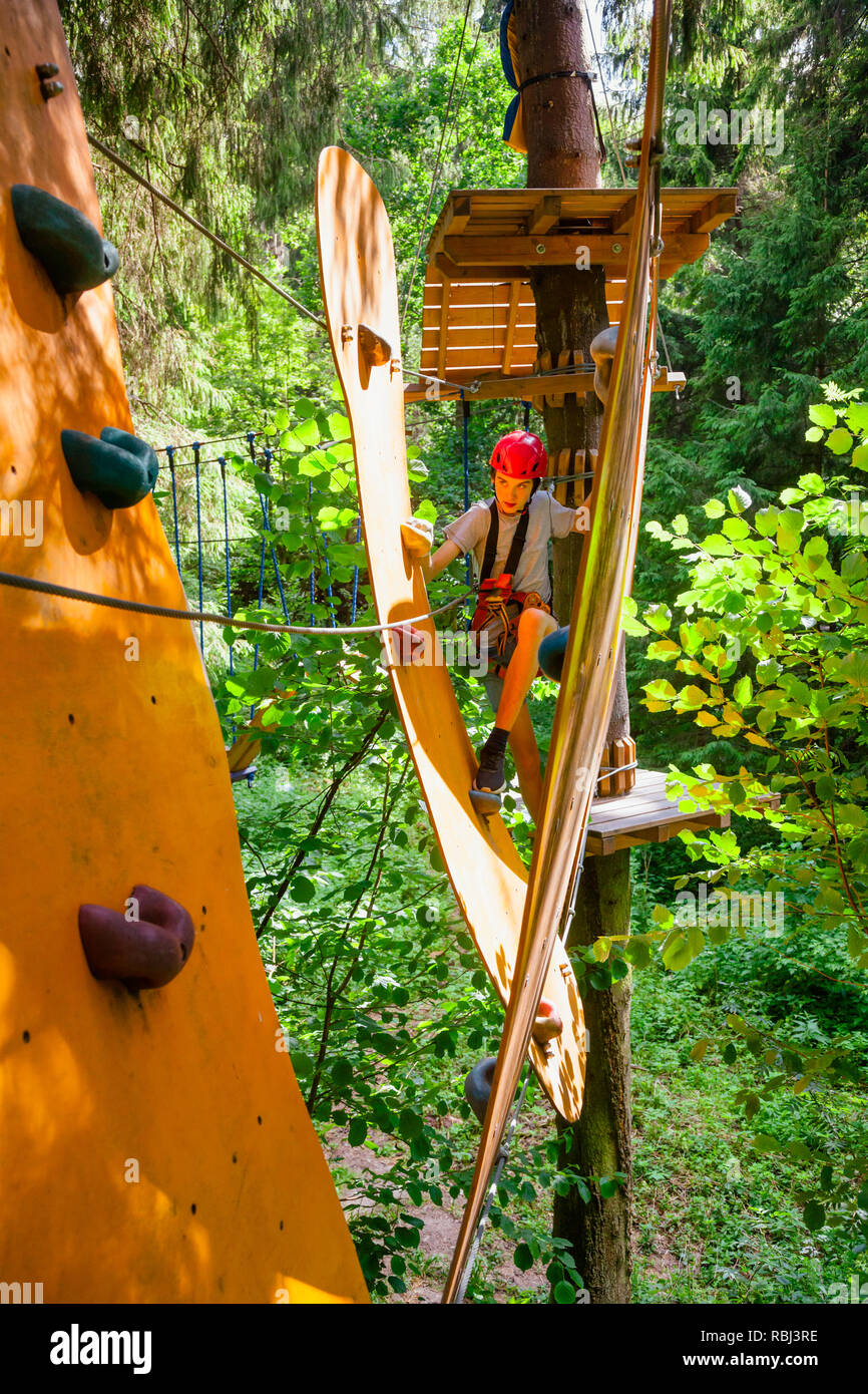 Teenager boy trug Gurt, Seil Brücke Hindernis zu einem Hochseilgarten im Outdoor treetop Adventure Park Stockfoto