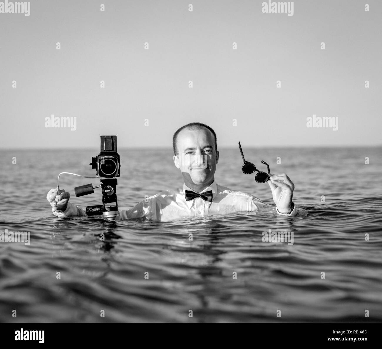Junge Fotograf im Wasser und halten Mittelformatkamera. Southampton Beach, New York, US 40-45 Jahre, 45-50 Jahre, 50-59 Jahre, Stockfoto
