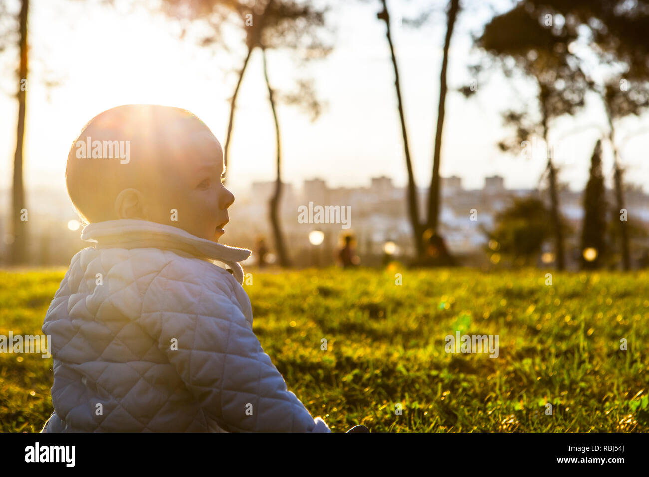 9 Monat Baby unter Sonnenstrahlen auf Gras Park. Vorteile des Sonnenlichts für Babys Konzept Stockfoto