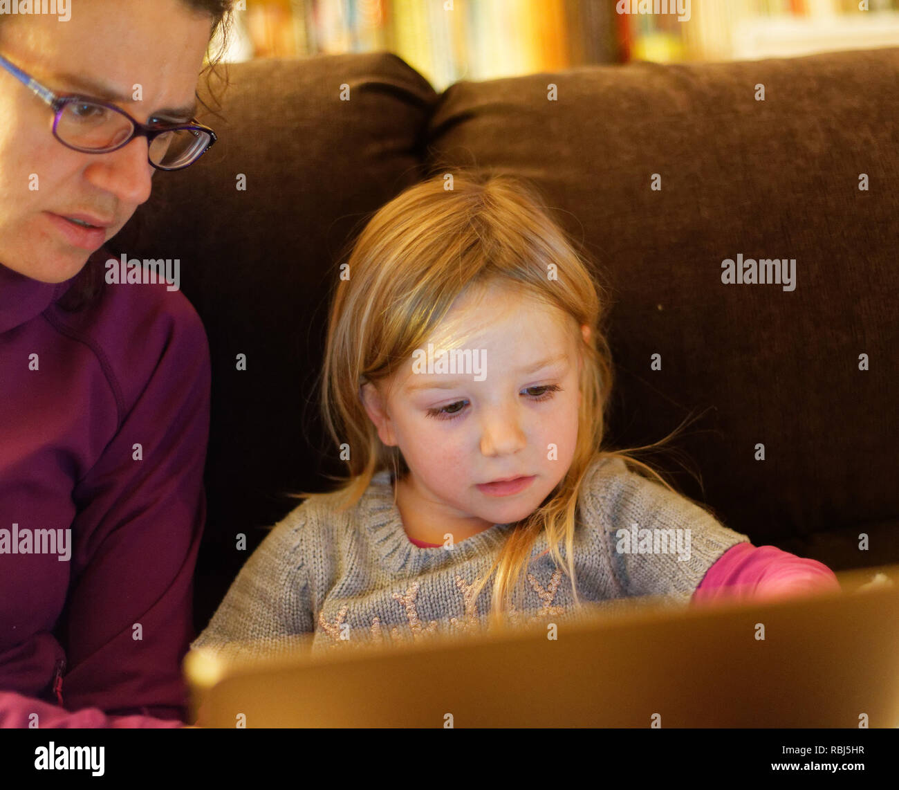 Ein kleines Mädchen (4 Jahre alt) und ihre Mutter saß auf einem mit einem Laptop Computer sofa zusammen Stockfoto