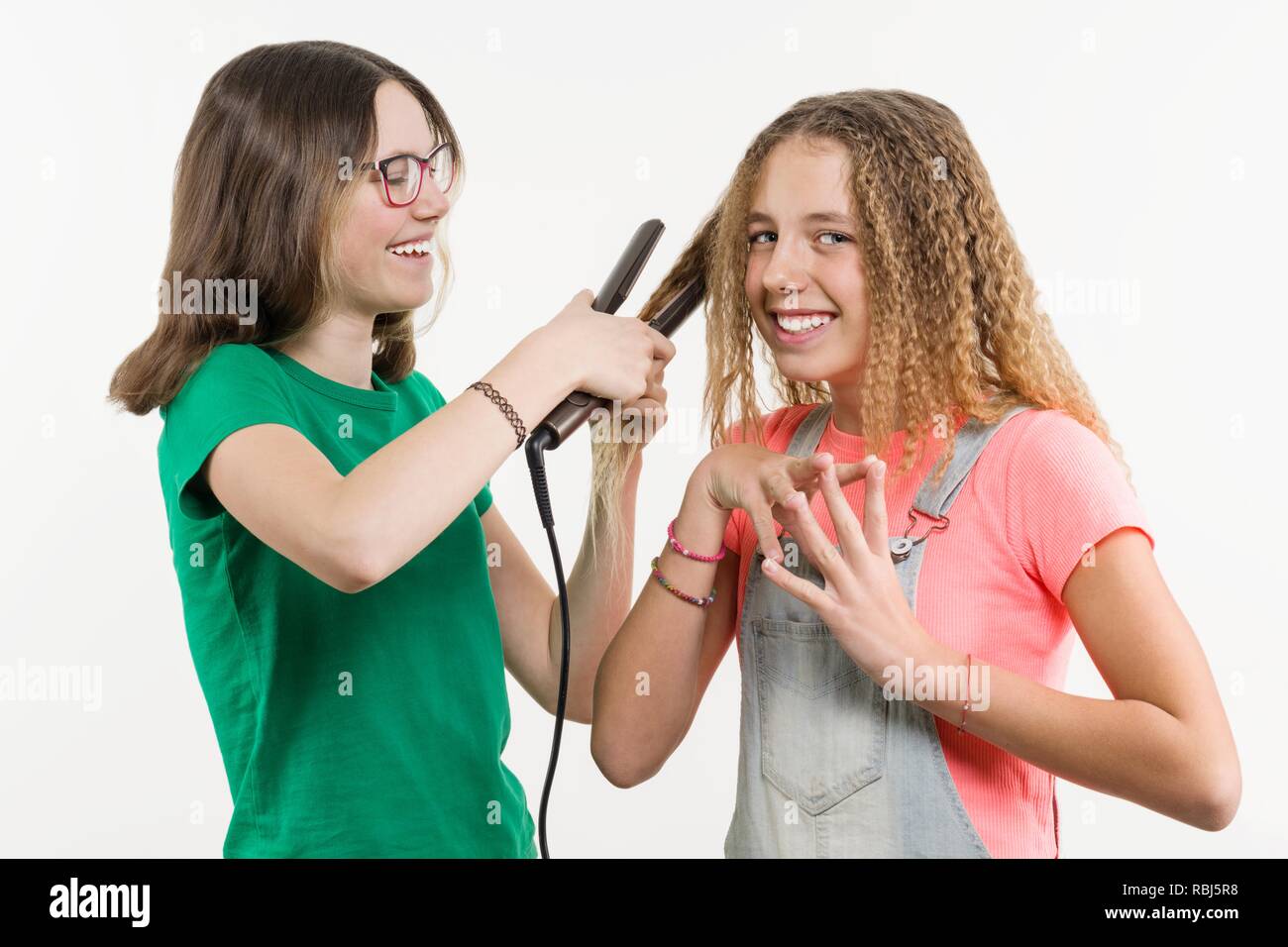 Portrait von zwei Jugendlichen Freundinnen Haarschnitt zuhause tun. Weißer Hintergrund, Mädchen, Emotion, Haarglätter. Stockfoto