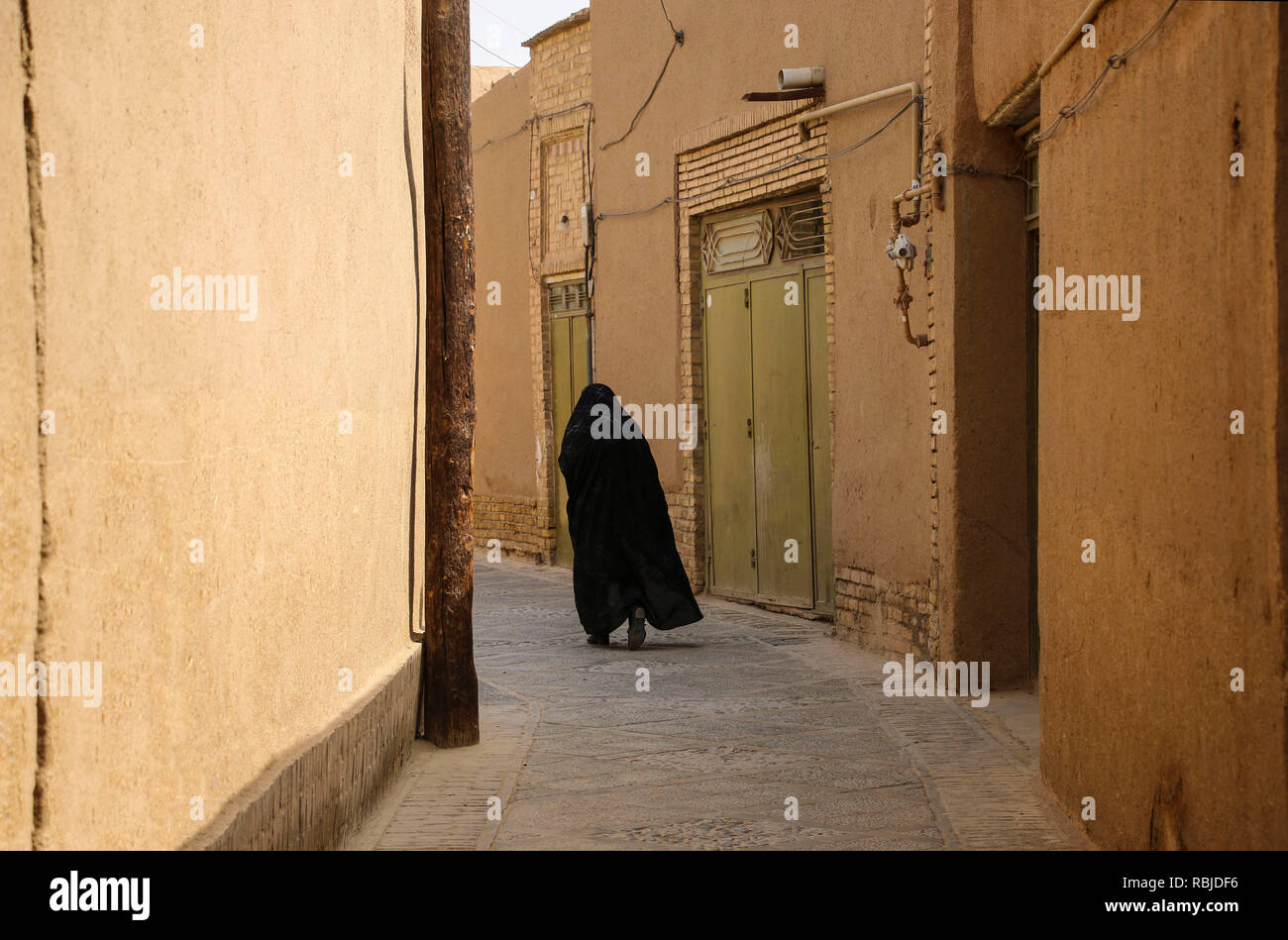 Muslimische Frau, in schwarz Spaziergang auf der schmalen Straße der alten Stadt Yazd, Iran gekleidet. Stockfoto