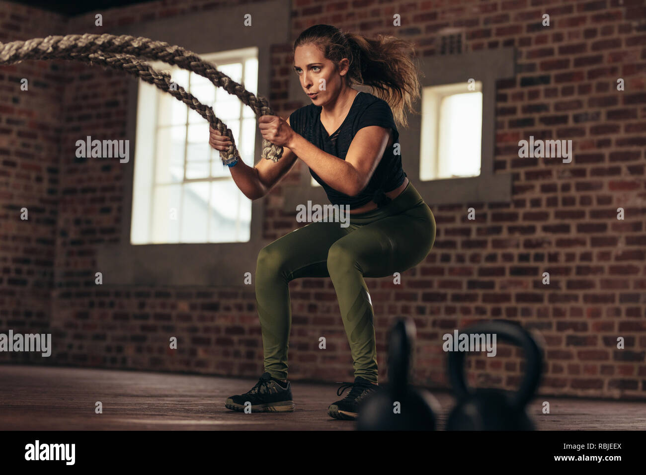 Fitness-Frau benutzt Kampfseile zum Training. Frauen trainieren mit Kampfseilen im Cross-Training-Fitnessstudio. Stockfoto