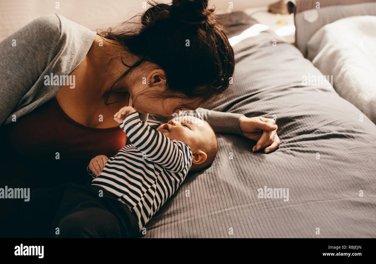 Frau mit ihr Baby auf ein Bett zu Hause liegen. Mutter pflegen und verwöhnen ihr Baby. Stockfoto