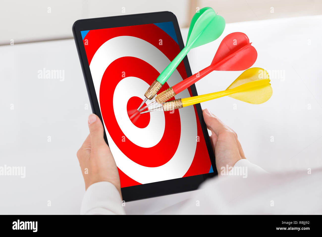 Die menschliche Hand Digital Tablet mit bunten Darts Target über Weiß Schreibtisch Stockfoto