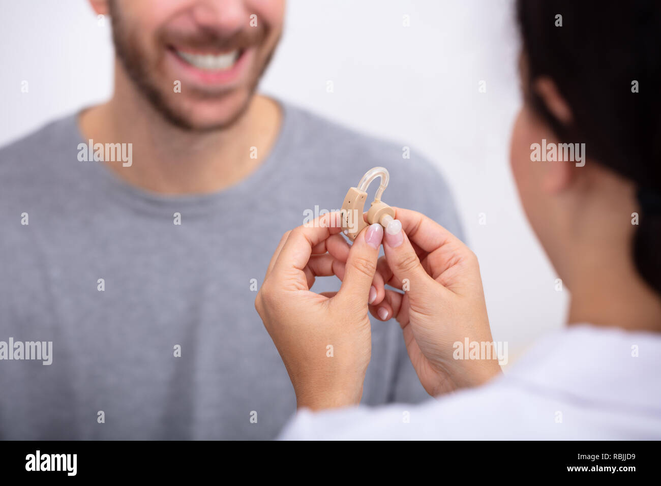 Junge männliche Patienten Betrachten Ärztin Holding Hörgerät In der Klinik Stockfoto