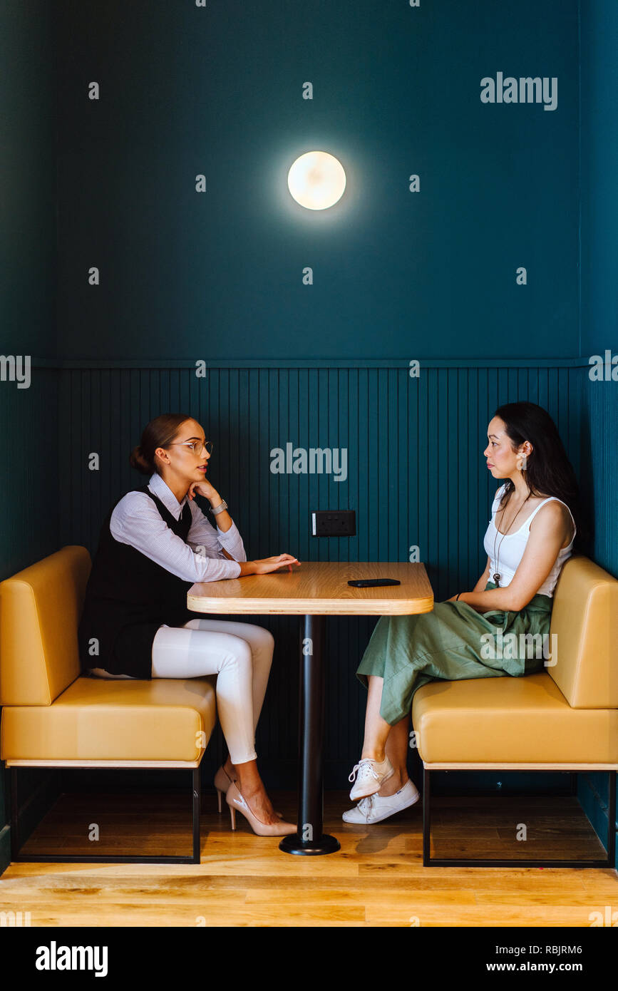 Zwei junge Frauen aus einem Anlauf haben ein Arbeitstreffen in einer trendigen Stand in Ihrem Büro während des Tages. Man ist im Kaukasus und den anderen asiatischen Chinesisch. Stockfoto