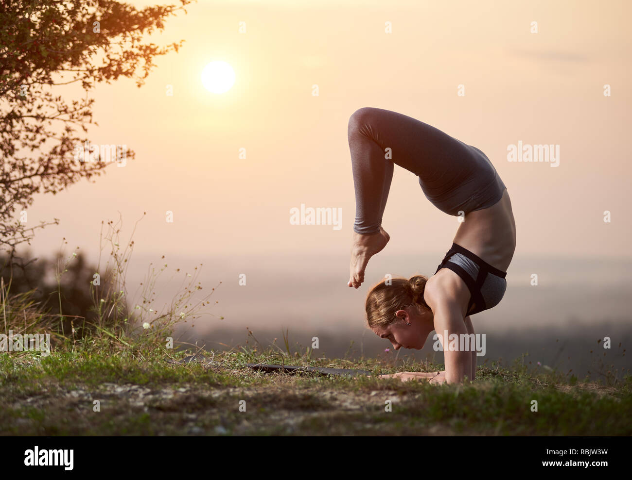 Attraktiver barfuss gymnast Frau in Trainingsanzug Ausbildung komplizierte Yoga Übungen im Freien auf Kopie Raum Hintergrund von hellrosa Sommer sogar Stockfoto