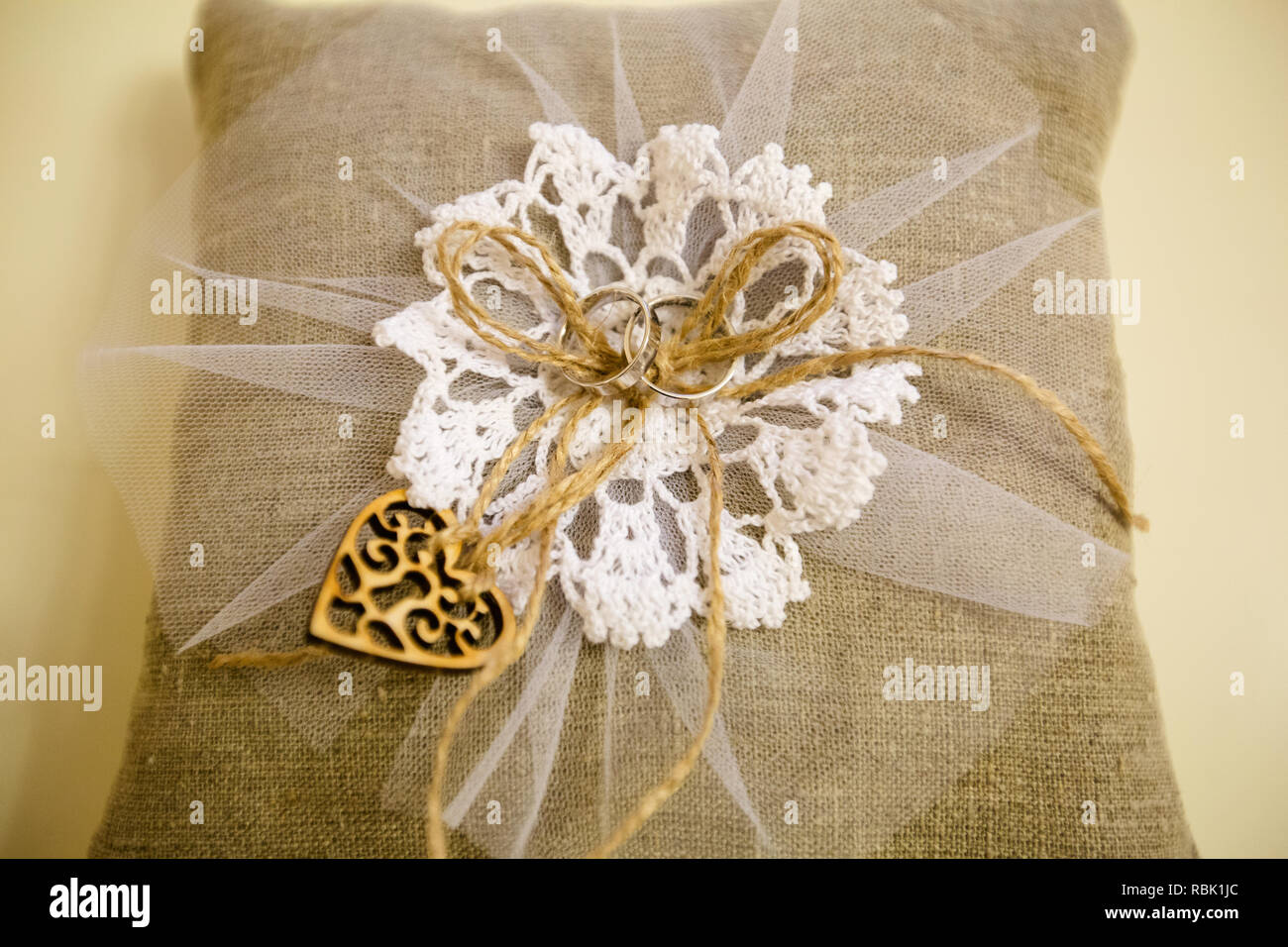 Ein paar Trauringe auf eine Leinwand mit Kissen. Die Oberseite der Kissen ist mit einem weißen Stoff Muster eingerichtet. In der Mitte ist ein Garn mit einer Schleife gebunden. Stockfoto