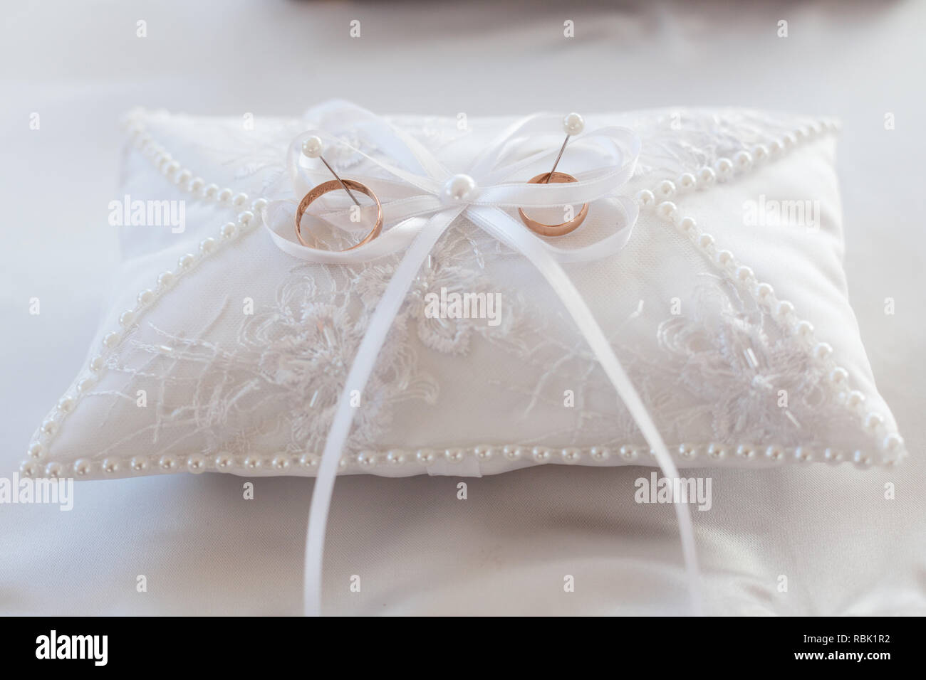 Ein paar Trauringe auf einem weißen Kissen. In der Mitte des Kissens ist eine Schleife. Close-up Stockfoto