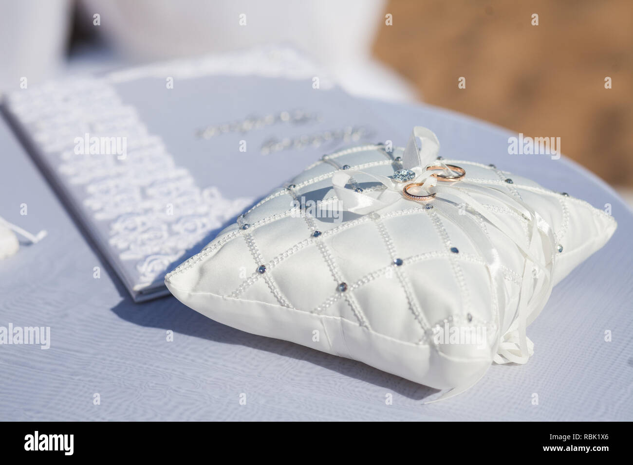 Ein paar Trauringe auf einem weißen Kissen. Ringe ineinander White Ribbon. Stockfoto