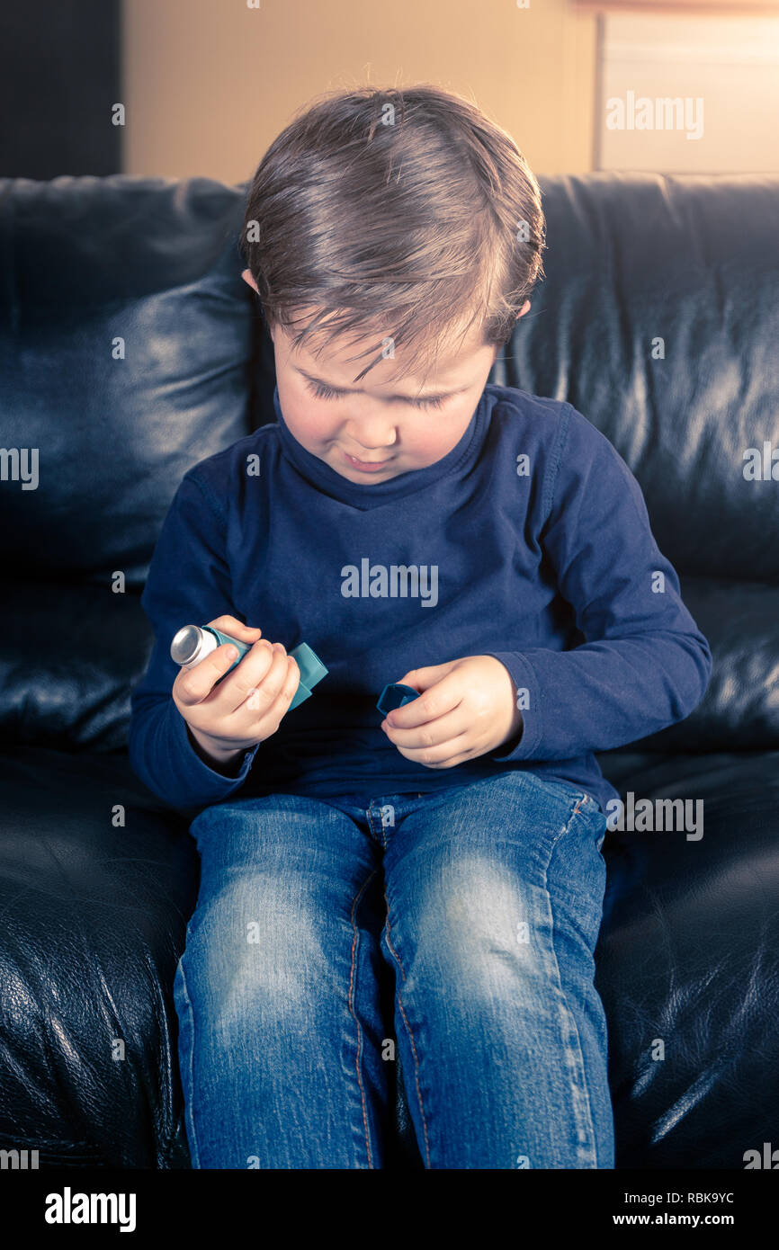 Süße 5 Jahre alten Jungen, die Kappe von Asthma Inhalator, sitzen in schwarzem Leder Sofa Stockfoto