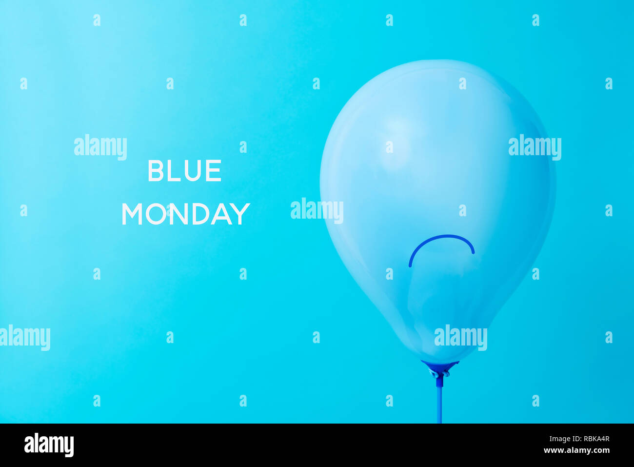 Nahaufnahme von einem blauen Ballon, mit einem traurigen Gesicht in es gezeichnet, und der Text blau Montag auf einem blauen Hintergrund Stockfoto