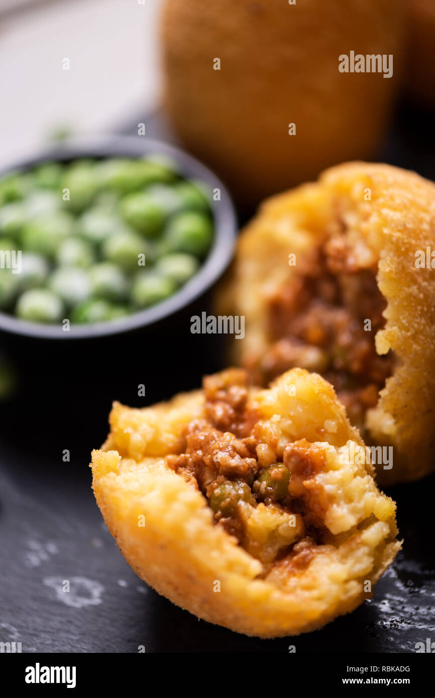 Nahaufnahme von arancini Reis Fleisch Ball Teller schwarz Servierteller mit frischen Erbsen und Basilikum auf rustikalen Tisch. Stockfoto