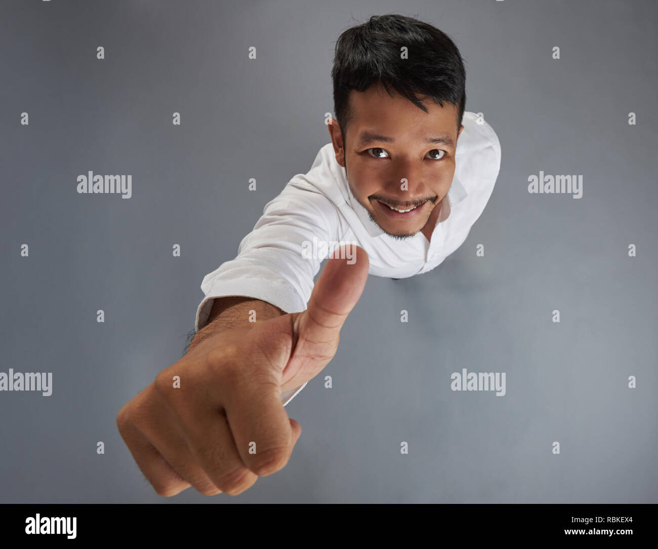 Lächelnd asiatischer Mann mit dem Daumen oben auf Grau studio Hintergrund isoliert Stockfoto