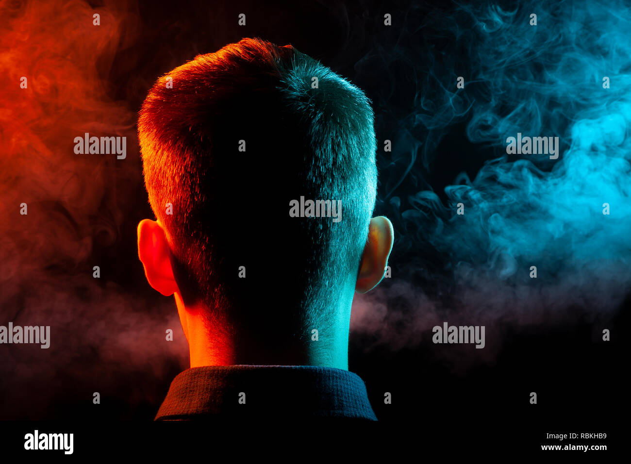 Ein Blick von hinten auf den Kopf eines Mannes in einem T-Shirt Rauchen eine vape und Ausatmen mehrfarbige Rauch von Grün und Rot in verschiedenen Richtungen von ihm Stockfoto