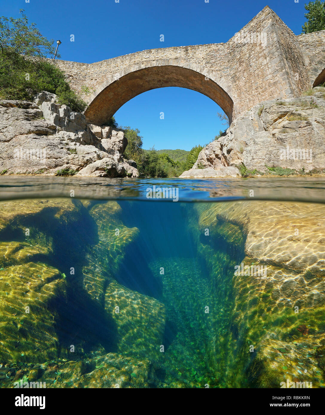 Fluss mit einer alten Steinbrücke und erodierten Felsen unter Wasser, geteilte Ansicht Hälfte oberhalb und unterhalb der Wasseroberfläche, Sant Llorenc de la Muga, Katalonien, Spanien Stockfoto