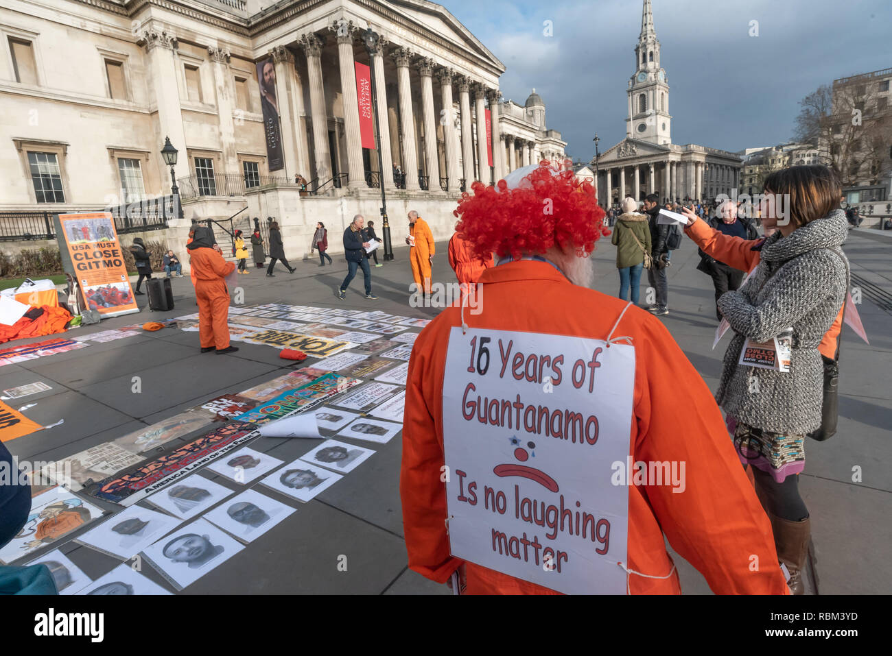 London, Großbritannien. 11. Januar 2019. Ein Mann in einem Clown Kopfbedeckung hat die Nachricht auf seinem Rücken" 16 Jahre Guantanamo ist keine lachende Angelegenheit' an der Protest von Guantanamo Gerechtigkeit Kampagne und London Guantanamo Kampagne markiert den 17. Jahrestag der ersten Gefangenen an der illegalen US-Camp ankommen. Eine Anzeige der Plakate, Fotografien der verbleibenden Häftlinge, Lesungen und Vorträge in Trafalgar Square markiert den Missbrauch, Folter, Menschenrechtsverletzungen, Zwangsernährung und unbegrenzte Haft gibt. Credit: Peter Marschall/Alamy leben Nachrichten Stockfoto