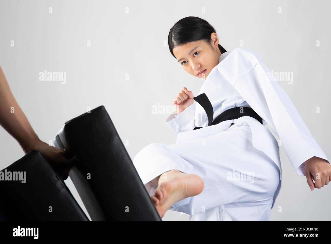 Junge schöne Frau mit Karate Anzug kicking mitt auf weißem Hintergrund Stockfoto