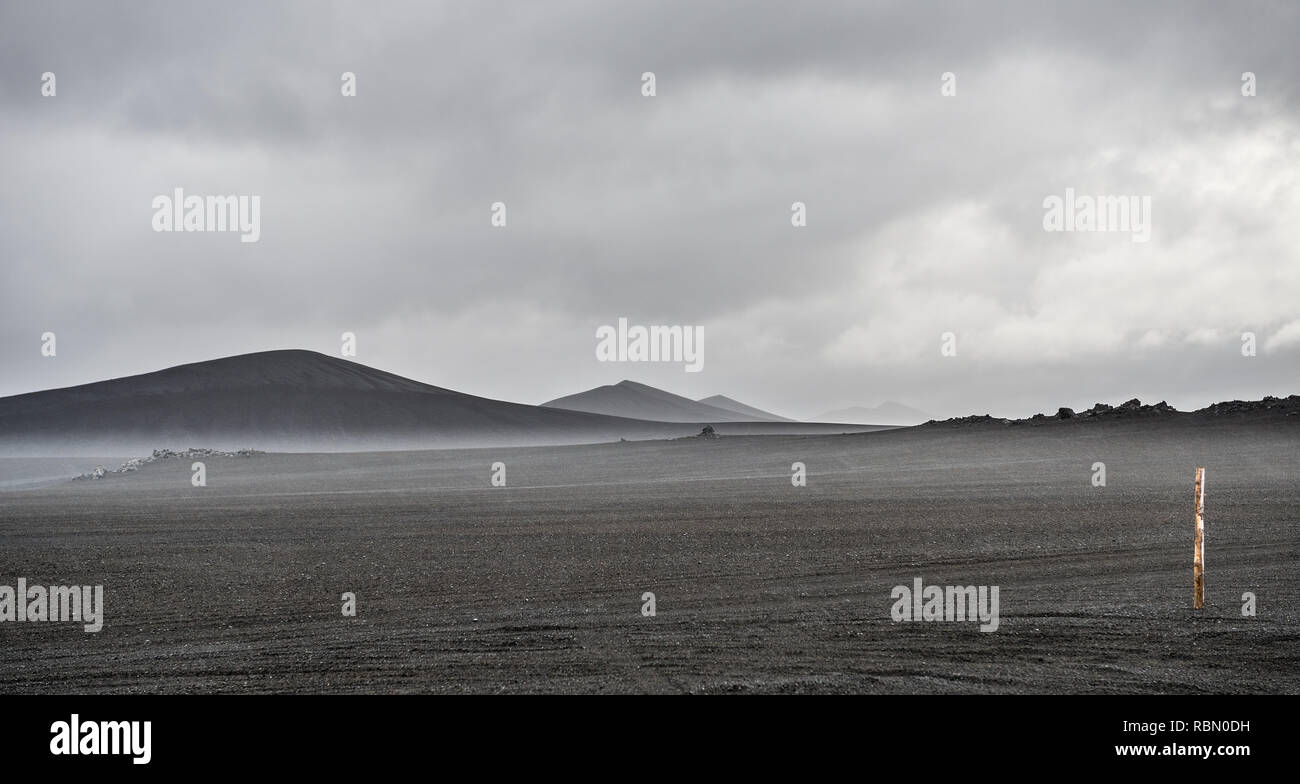 Einsame schwarze vulkanische Landschaft mit Kies, Nebel und Hügel Stockfoto