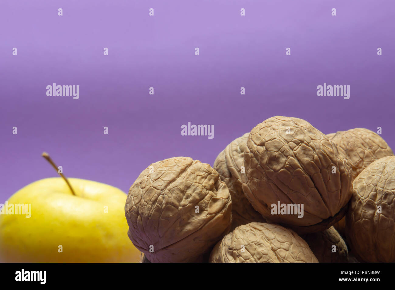 Gesamten gemeinsamen Walnüsse mit Schale in natürlichen Coconut shell Cup und gelber Apfel auf lila Hintergrund Stockfoto