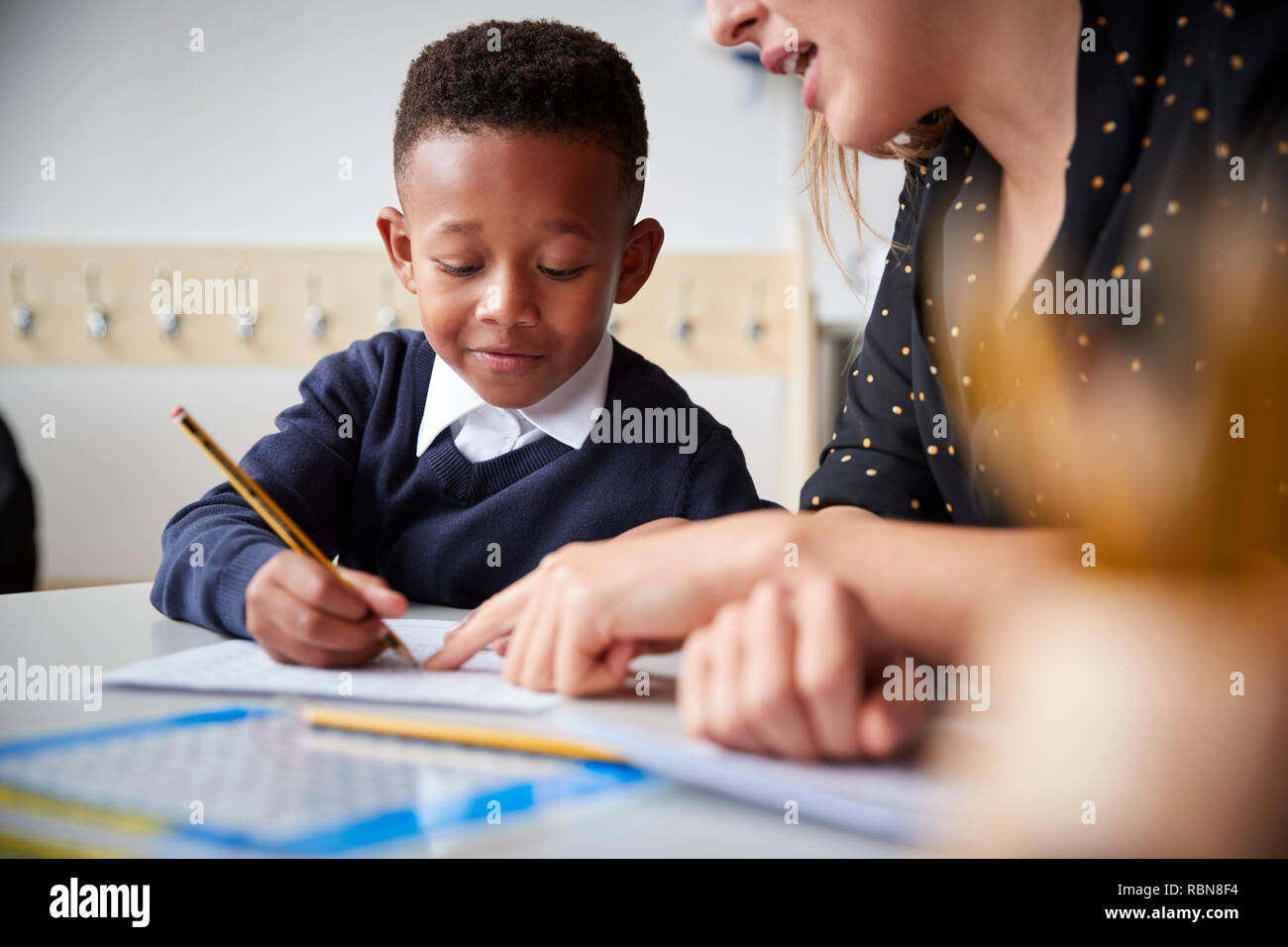 Weibliche Lehrer helfen, eine junge Schule Junge am Tisch in einem Klassenzimmer sitzen, Nahaufnahme, selektiver Fokus Stockfoto