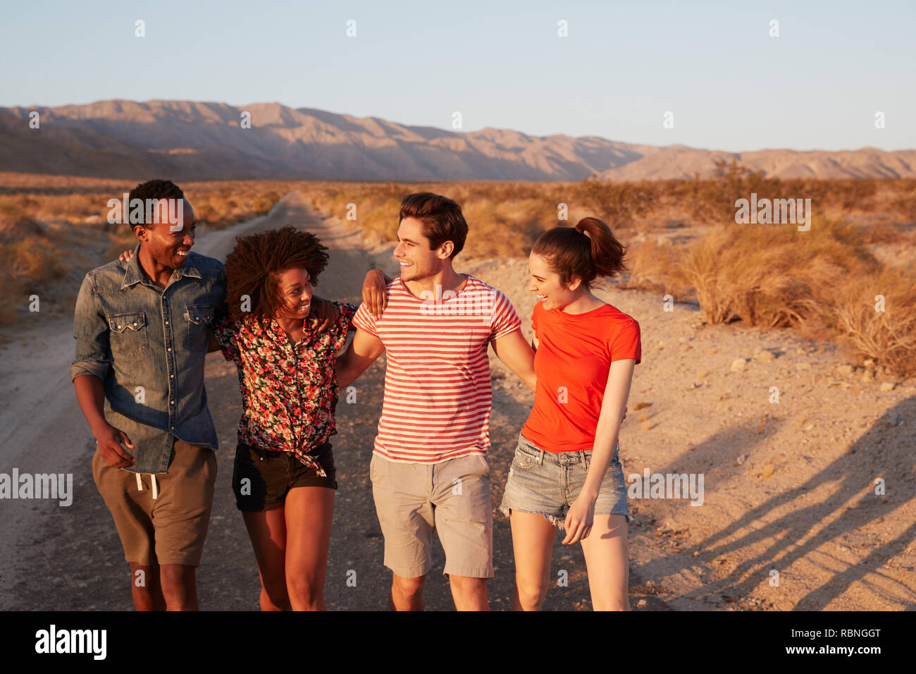 Vier junge erwachsene Freunde gehen auf eine Wüste Straße, in der Nähe Stockfoto