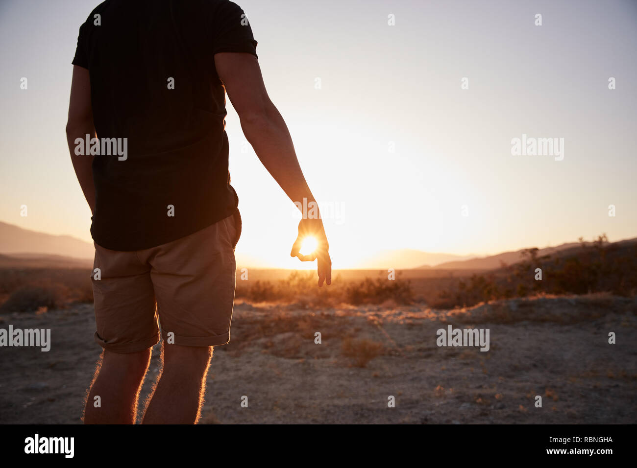 Mann in der Wüste Einkreisen der untergehenden Sonne mit Fingern, mittlerer Abschnitt Stockfoto