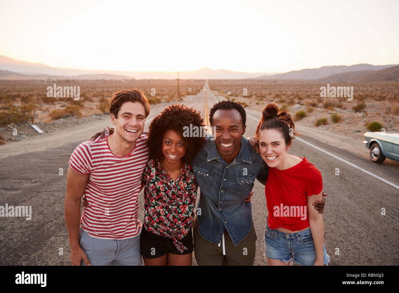 Vier Freunde auf einer einsamen Landstraße lächelnd in die Kamera, in der Nähe Stockfoto