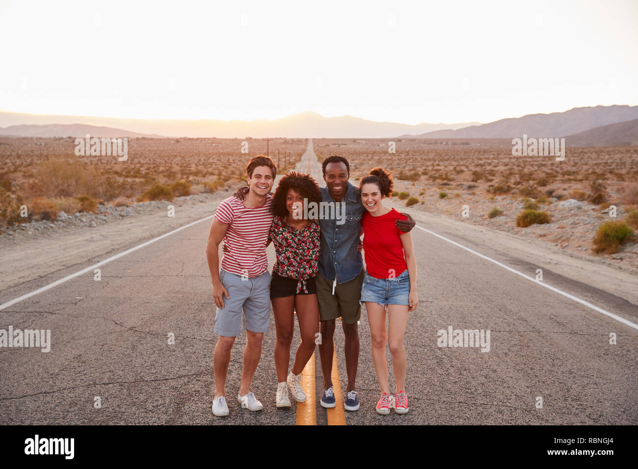 Vier Freunde stehen auf einer einsamen Landstraße lächelnd in die Kamera Stockfoto