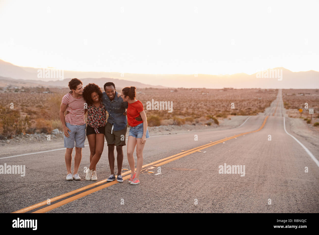 Vier junge erwachsene Freunde stehen auf desert Highway sprechen Stockfoto