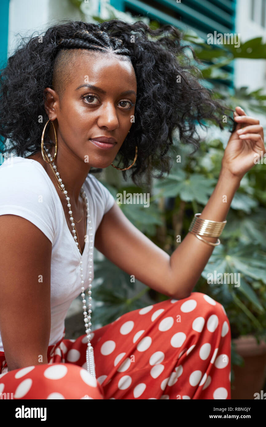 Junge schwarze Frau sitzt draußen und Ihr Haar berühren Stockfoto