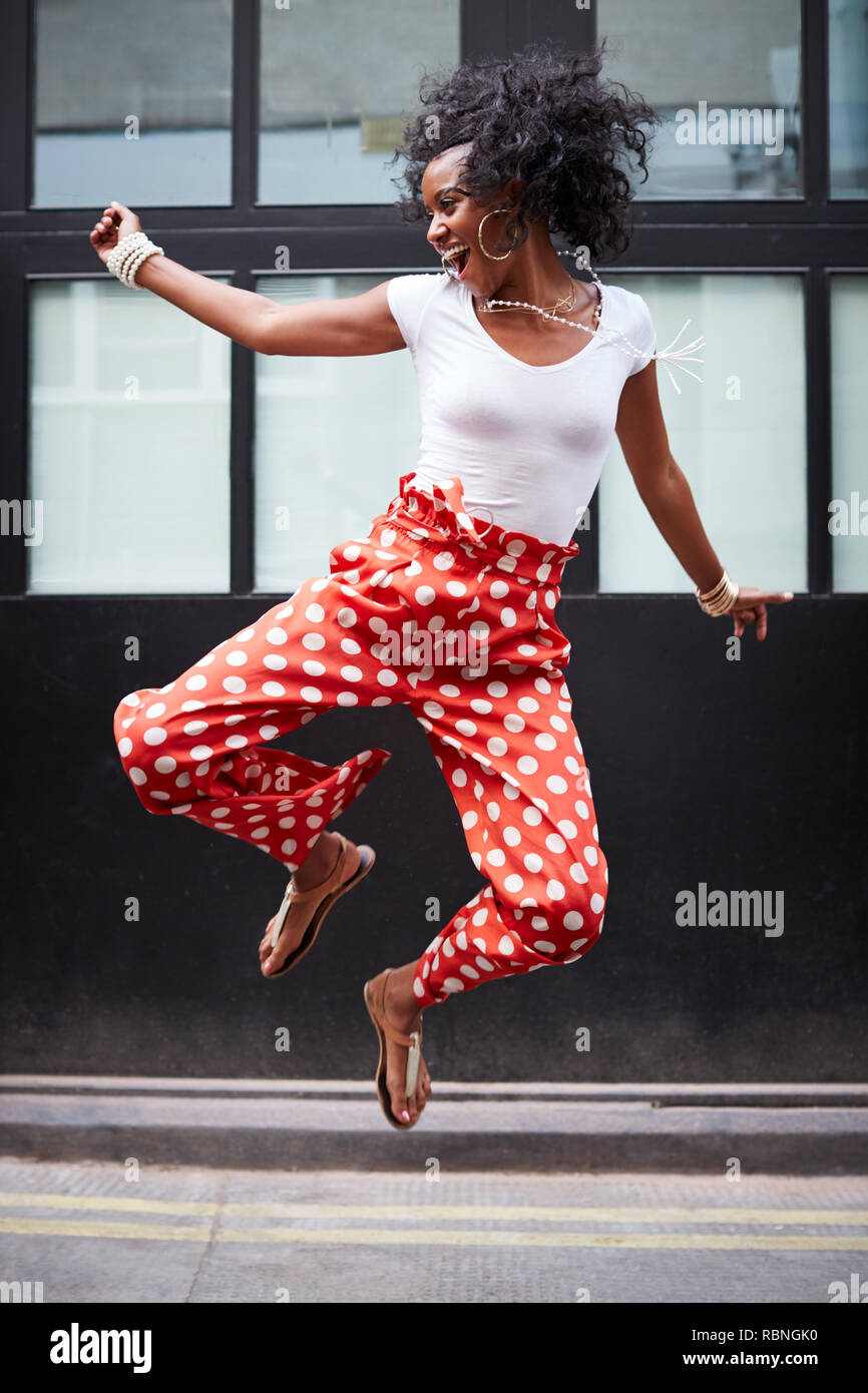 Modische junge Frau springt auf und lacht, volle Länge Stockfoto