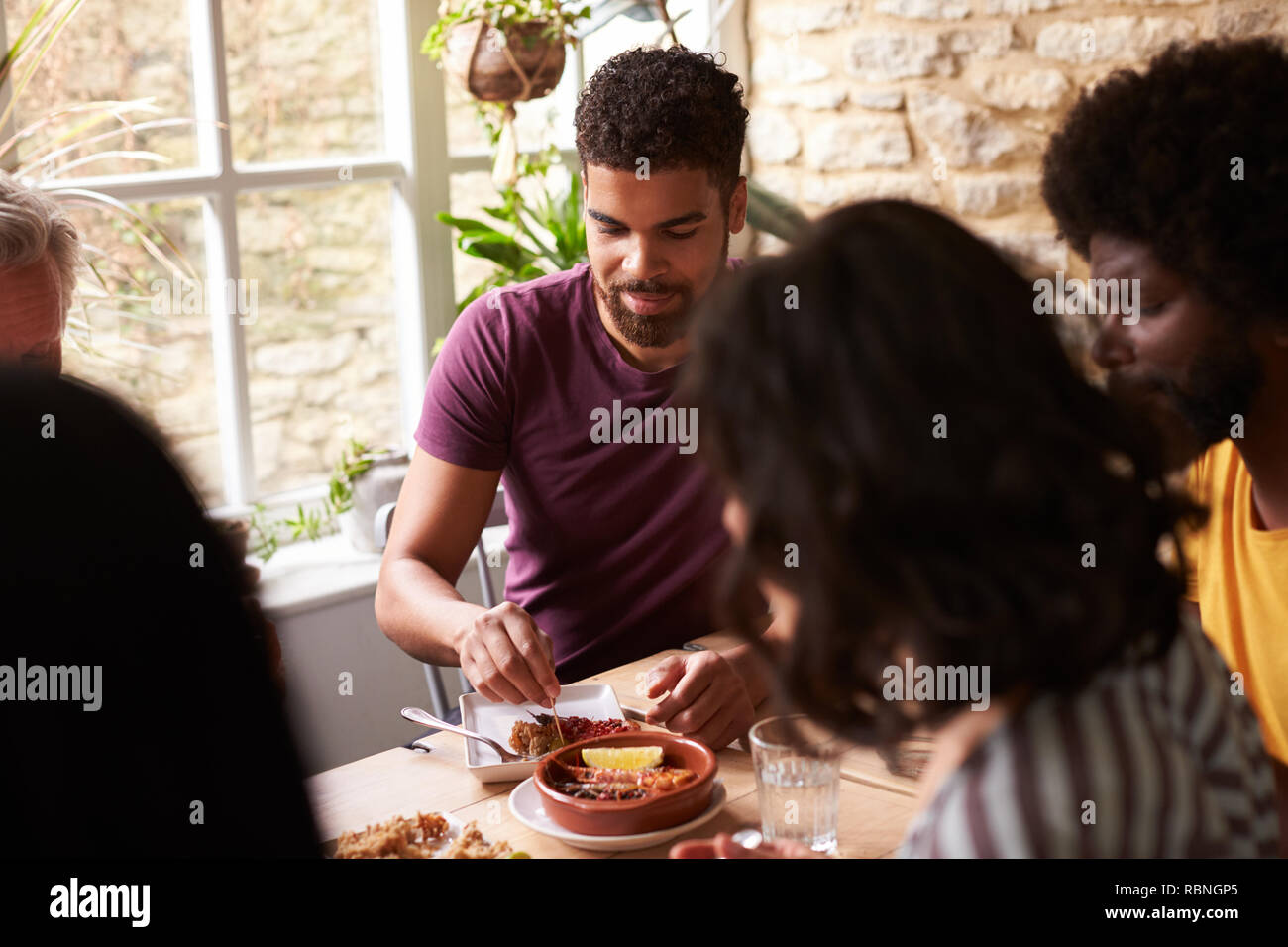 Junge gemischte Rasse Mensch essen mit Freunden an einem Esstisch Stockfoto