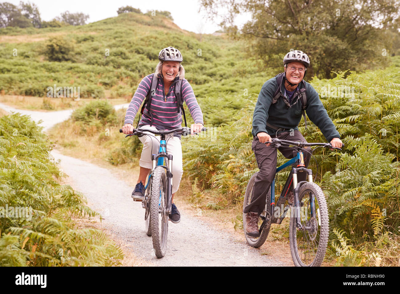 Senior paar Riding Mountain bikes in einem Feldweg bei einem Campingurlaub lächelnd, Vorderansicht Stockfoto