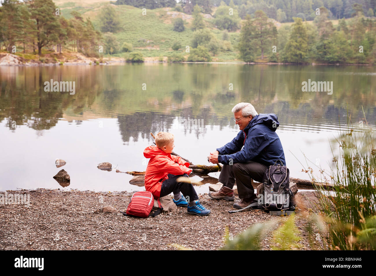 Großvater und Enkel am Ufer eines Sees sprechen, Sitzen, Erhöhte Ansicht, Lake District, Großbritannien Stockfoto
