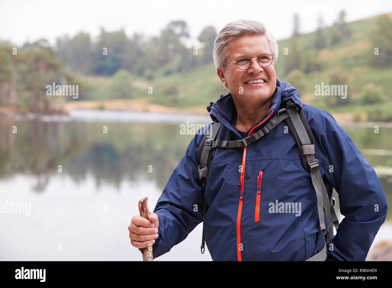 Im mittleren Alter Mann, der an einem See mit einem Stock, Lächeln, Nahaufnahme, Lake District, Großbritannien Stockfoto