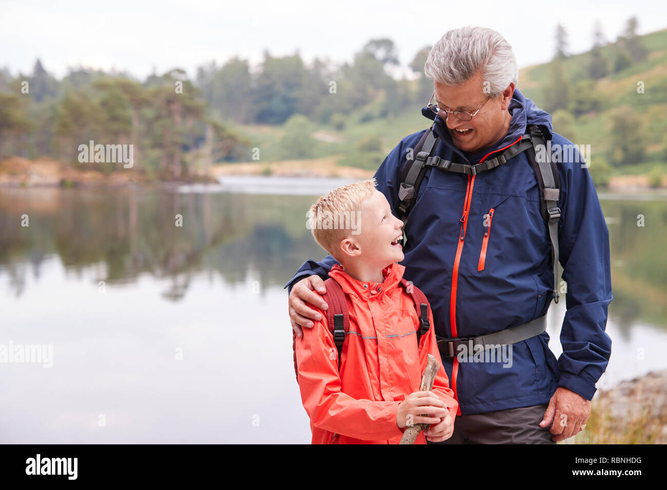 Großvater und Enkel stehen am Ufer eines Sees sich einander Lachen, Lake District, Großbritannien Stockfoto