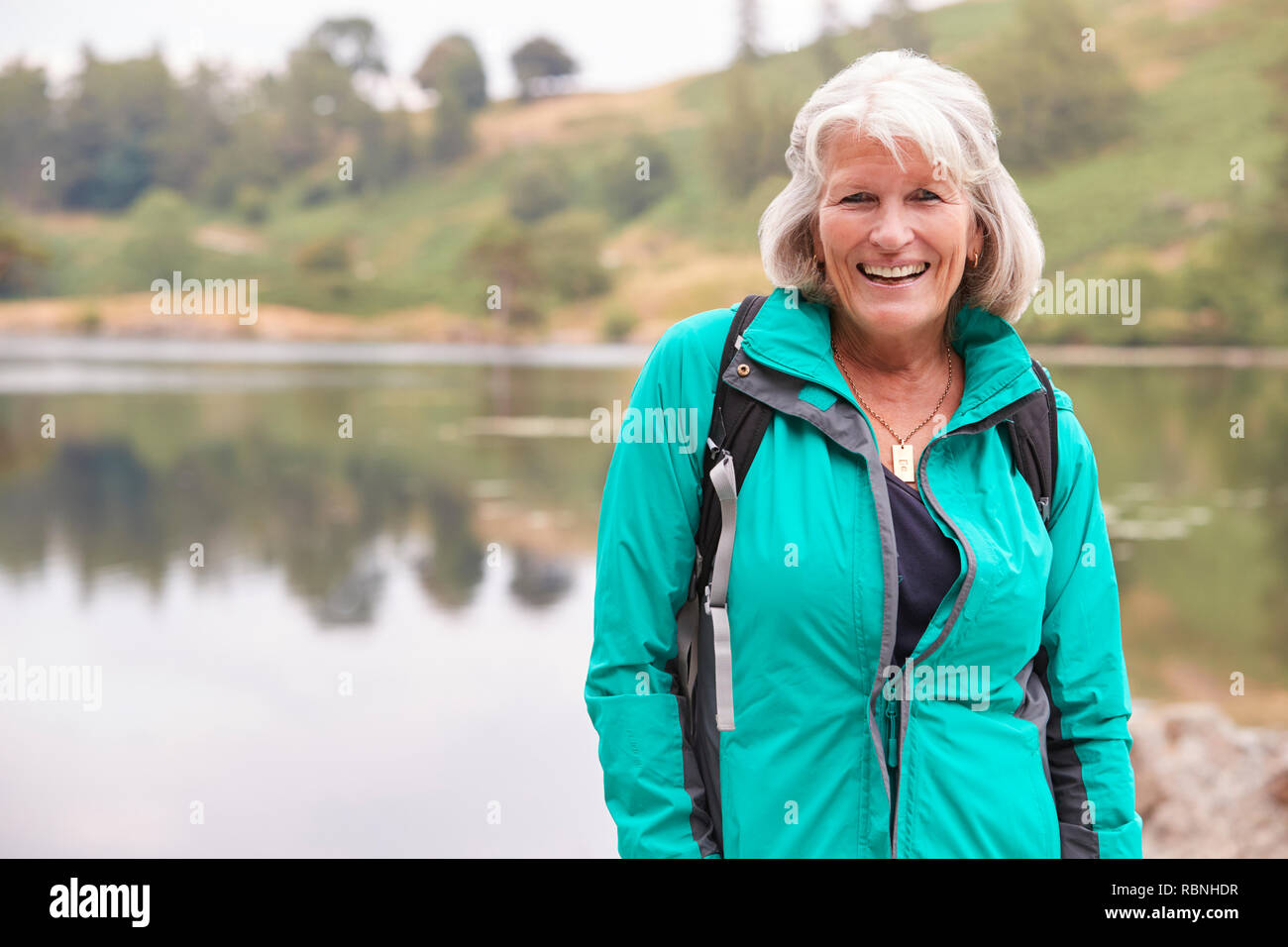 Senior kaukasische Frau, die an einem Ufer eines Sees lächelnd in die Kamera, Porträt Stockfoto