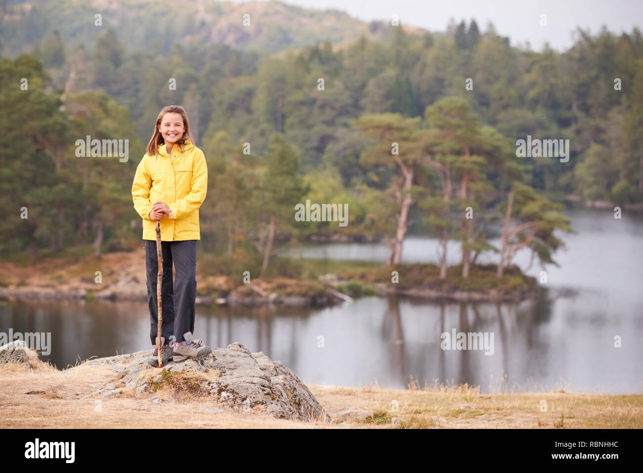 A vor - jugendlich Mädchen steht auf einem Felsen mit einem Stick, lächelnd in die Kamera, lakeside Hintergrund Stockfoto