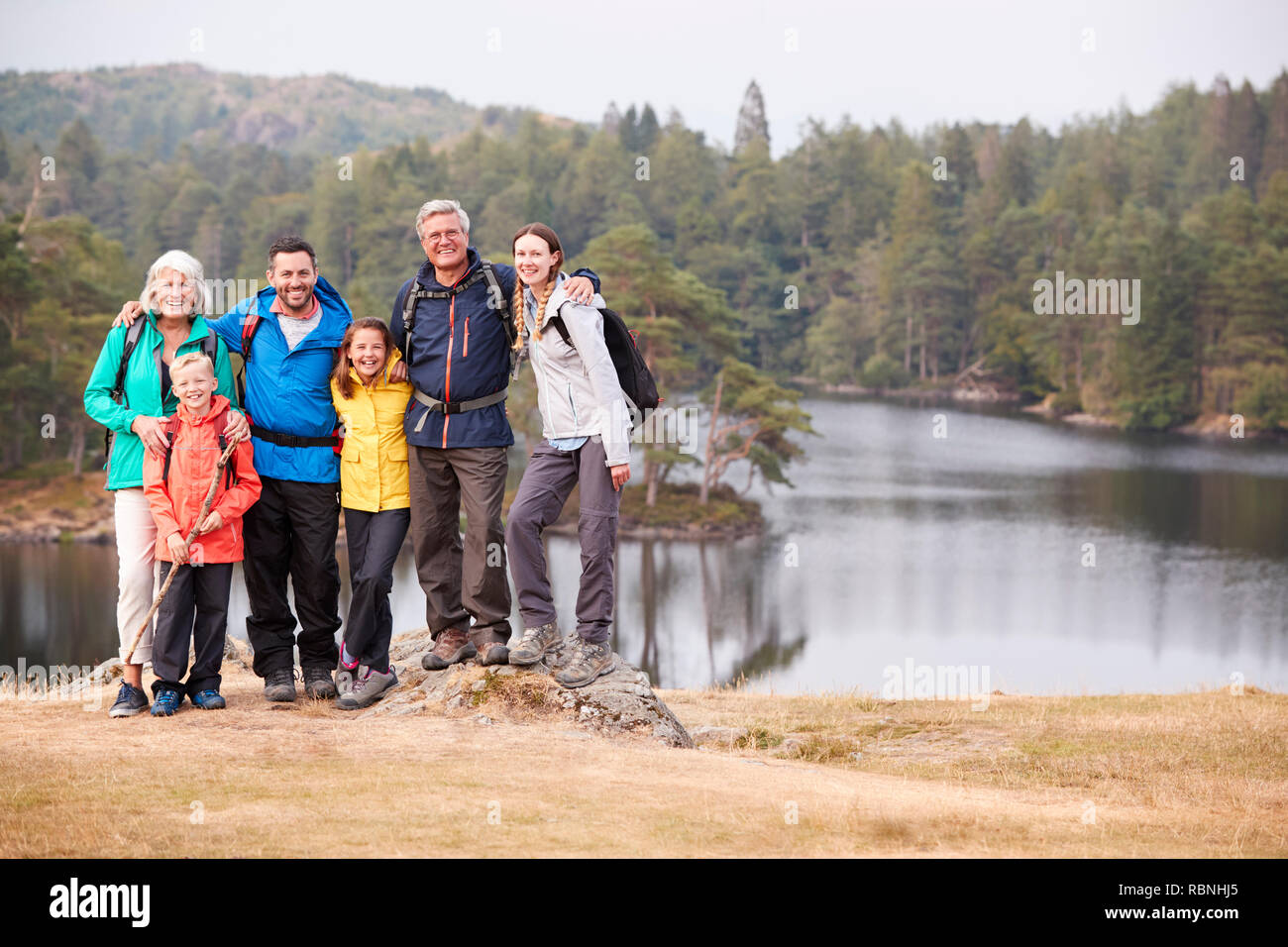 Multi-generation Familie stehen, an einem See, ein Lächeln für die Kamera, Vorderansicht, Lake District, Großbritannien Stockfoto