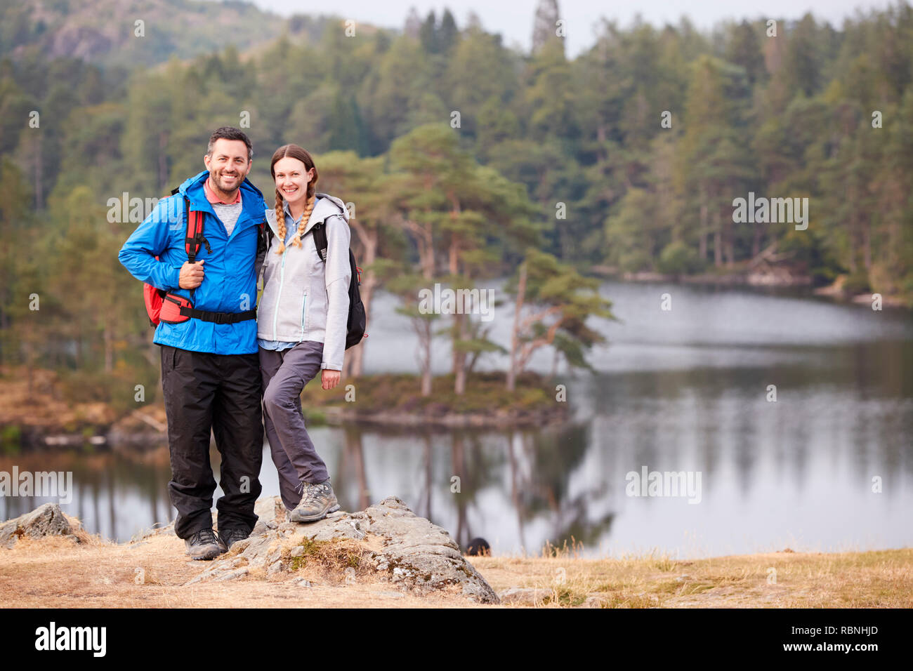 Junge Erwachsene Paar steht auf einem Felsen an einem See im Hinterland, Lächeln für die Kamera, volle Länge Stockfoto