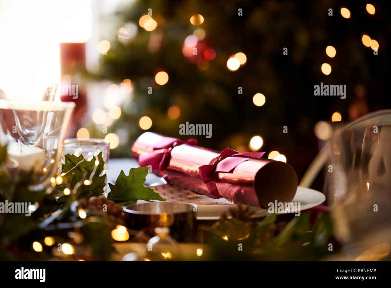 In der Nähe von Weihnachten Tabelle mit einem Christmas Cracker auf eine Platte und ein Weihnachtsbaum im Hintergrund angeordnet Stockfoto