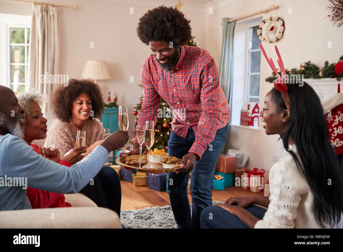 Mann mit Sekt und Snacks als Erwachsene Mitglieder der Familie Weihnachten feiern zu Hause Stockfoto