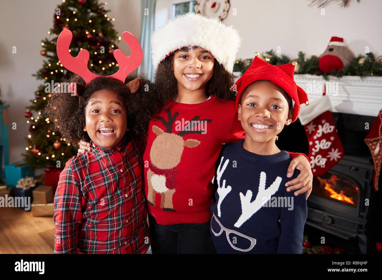 Portrait von Kindern tragen Festliche Jumper und Hüte feiern Weihnachten zu Hause zusammen Stockfoto