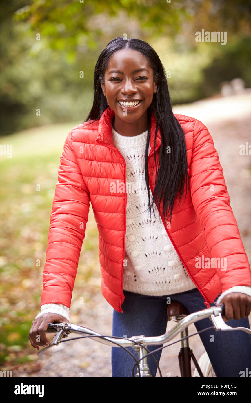 Junge Erwachsene schwarze Frau sitzt auf einem alten Fahrrad in einem Park lächelnd in die Kamera, Vorderansicht, in der Nähe Stockfoto